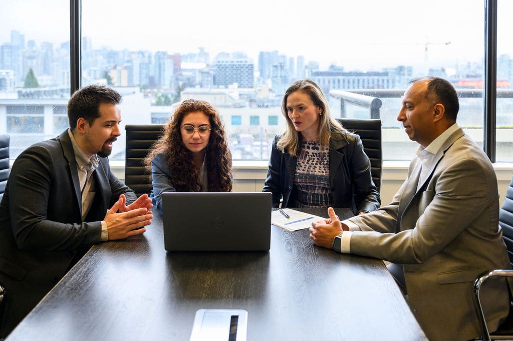 Professionals seated at table looking at laptop