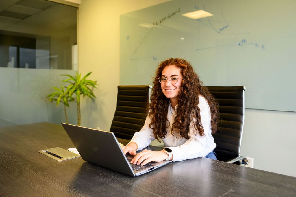 Woman seated in front of laptop smiling at camera